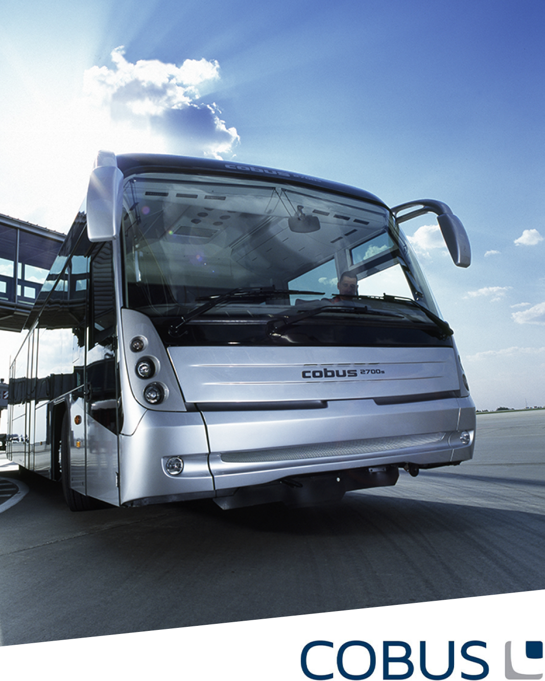 Ein moderner silberner Cobus 2700S Flughafen-Shuttlebus, hergestellt von Cobus Industries, steht auf einer Rollbahn unter einem blauen Himmel mit Wolken. Das COBUS-Logo erscheint in der unteren rechten Ecke des Bildes.